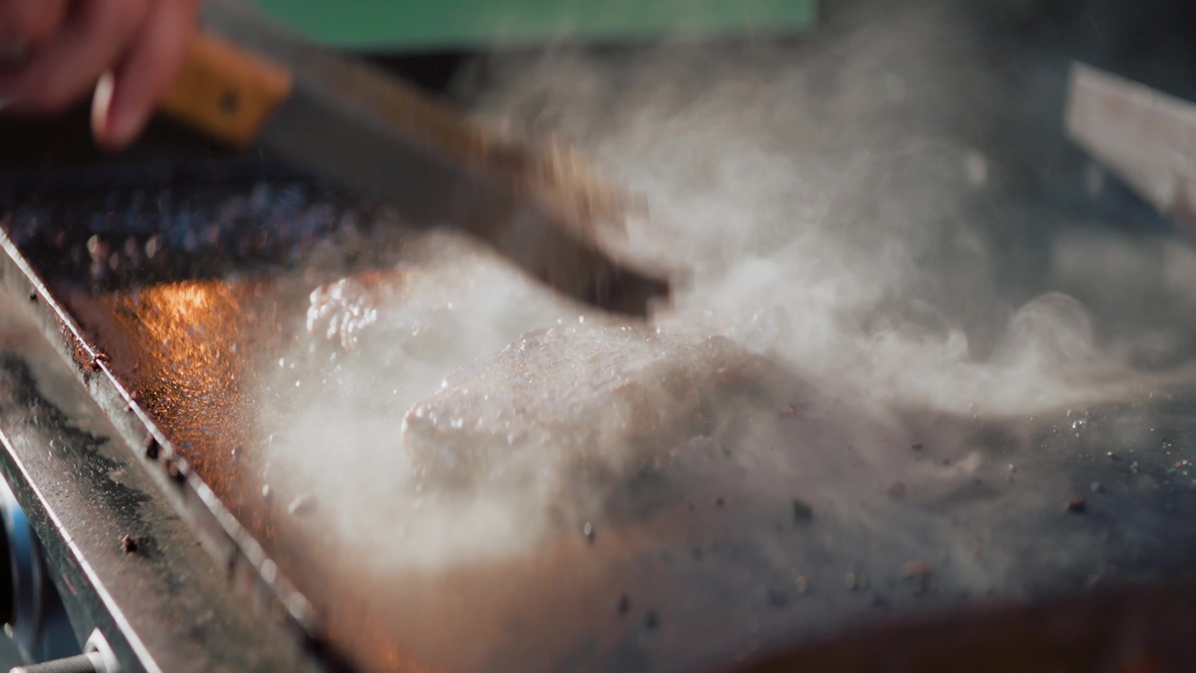 Steam rising off a hot flat-top griddle, backlit by string lights